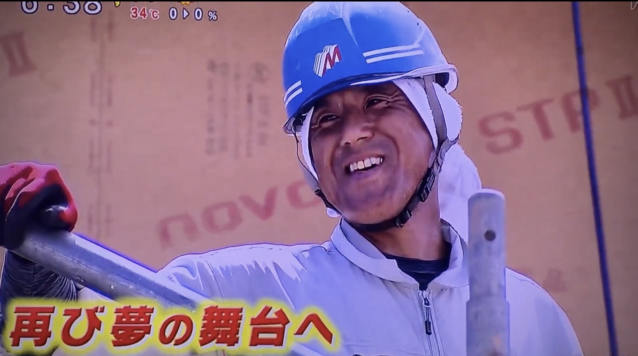 青い作業用ヘルメットをかぶり笑顔を見せる久野光博